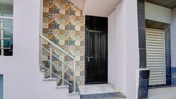 A staircase with a metal railing leading to a black door, a tiled wall with geometric patterns, and a closed shutter door. - Classic Gomti Nagar Station (Lucknow)