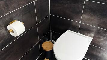 A modern bathroom with dark tiles, a toilet, a bidet, and a toilet paper holder.