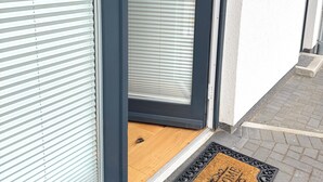 A modern building entrance with a glass door, a doormat with 'WELCOME' text, and a keypad lock.