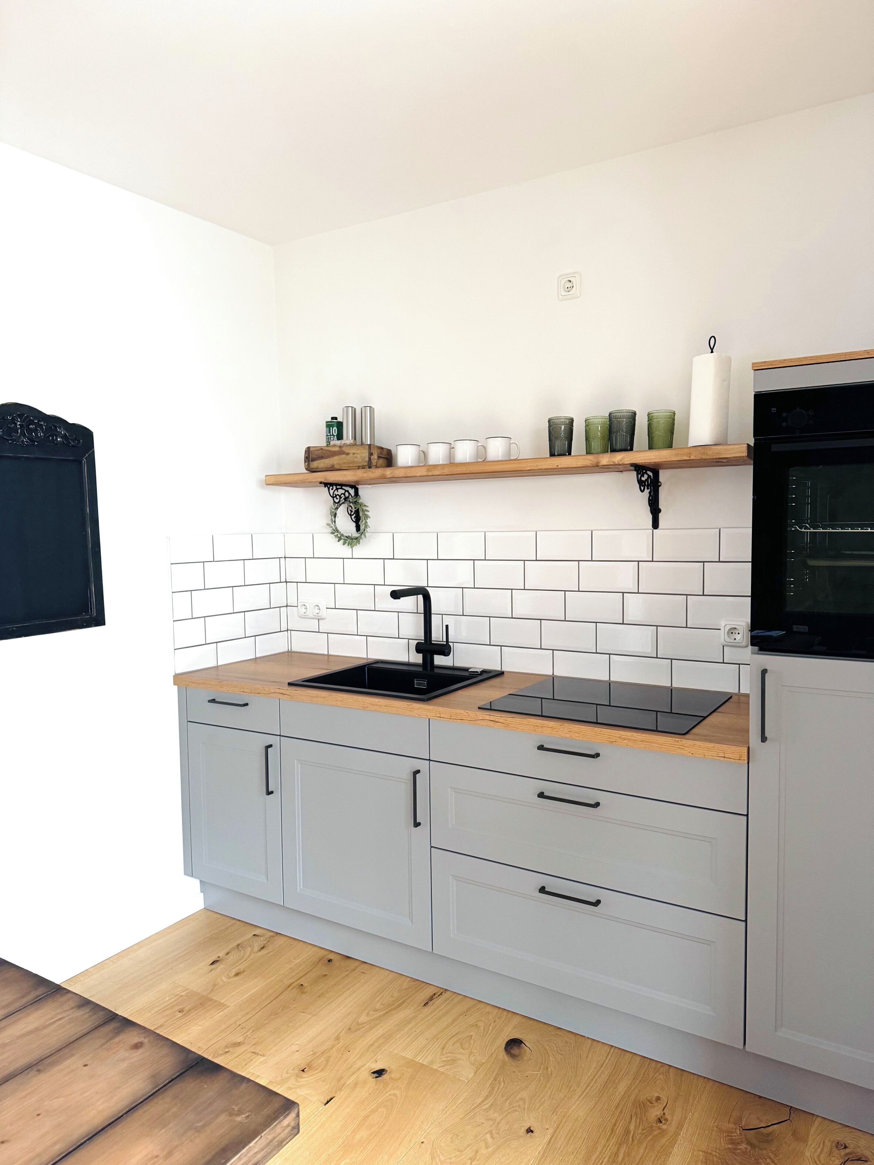 A kitchen with white cabinets, a wooden countertop, a black sink, and a built-in oven.