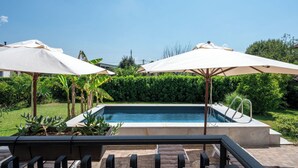 Piscina com duas guarda-sóis, cadeiras de lounge e vista para o jardim.