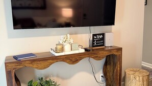 Un tavolo consolle in legno con una TV a schermo piatto montata sopra, una piccola pianta in vaso e un cartello decorativo.