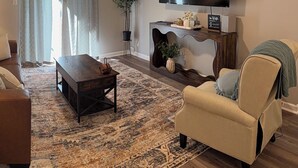 Un soggiorno con un divano, un tavolino, una televisione, una ventola a soffitto e un grande tappeto.
