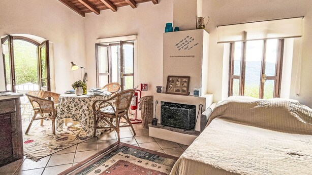 Una camera accogliente con soffitto in legno, un'area pranzo con sedie in vimini, un caminetto e un letto.