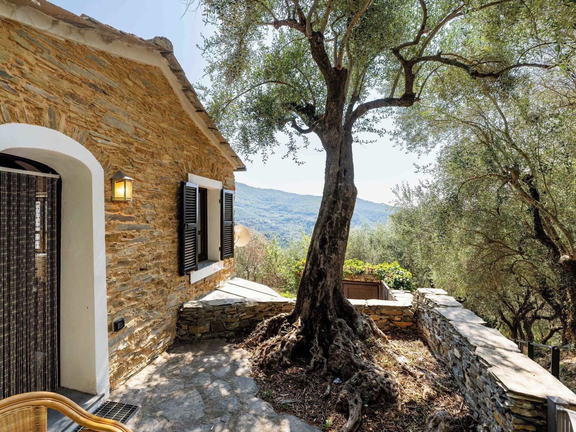 A stone building with a large tree in front, a stone wall, and a view of the landscape.