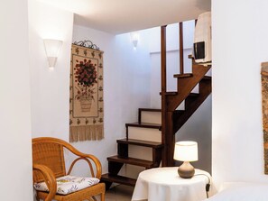 Eine Treppe mit hölzernen Stufen und einem an der Wand befestigten Fernseher. Ein Korbstuhl mit Kissen steht in der Nähe der Treppe, und ein Tisch mit einer Lampe befindet sich auf der Wendeltreppe.