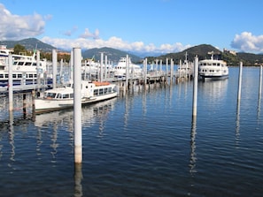 A marina with boats docked at wooden piers, calm water, and a mountainous landscape in the background.
