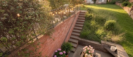 Un patio jardín con mesa de madera, plantas en macetas y pared de ladrillo.