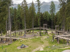Ein bewaldetes Gebiet mit einer Holzbrücke, einem Spielplatz und Picknicktischen.