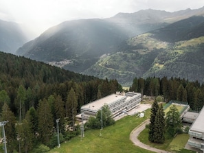 A modern building with a flat roof, surrounded by dense forest and mountains. - Beautiful apartment for 4 people with WIFI, TV and balcony (Mezzana)