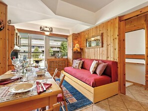 Ein gemütliches Zimmer mit Holzboden, einem roten Sofa, einem Esstisch, der mit Tellern und Gläsern gedeckt ist, und einem Fenster mit Blick auf Gebäude.