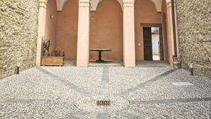 Un cortile con mura in pietra, archi, un tavolo e una fioriera.