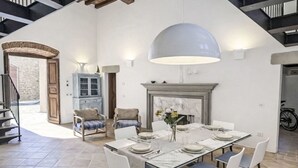 Zona pranzo con tavolo in marmo, sedie bianche, una grande lampada a sospensione e un camino.