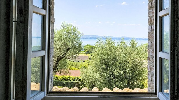 Una finestra aperta con vista su un paesaggio che include alberi e un corpo d'acqua.
