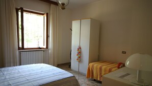 Ein Schlafzimmer mit Bett, Kleiderschrank, Heizkörper und Schreibtisch mit Lampe.