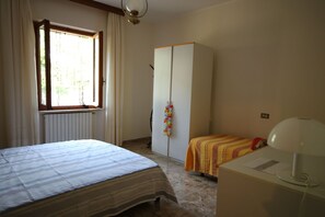 Ein Schlafzimmer mit Bett, Kleiderschrank, Heizkörper und Schreibtisch mit Lampe.