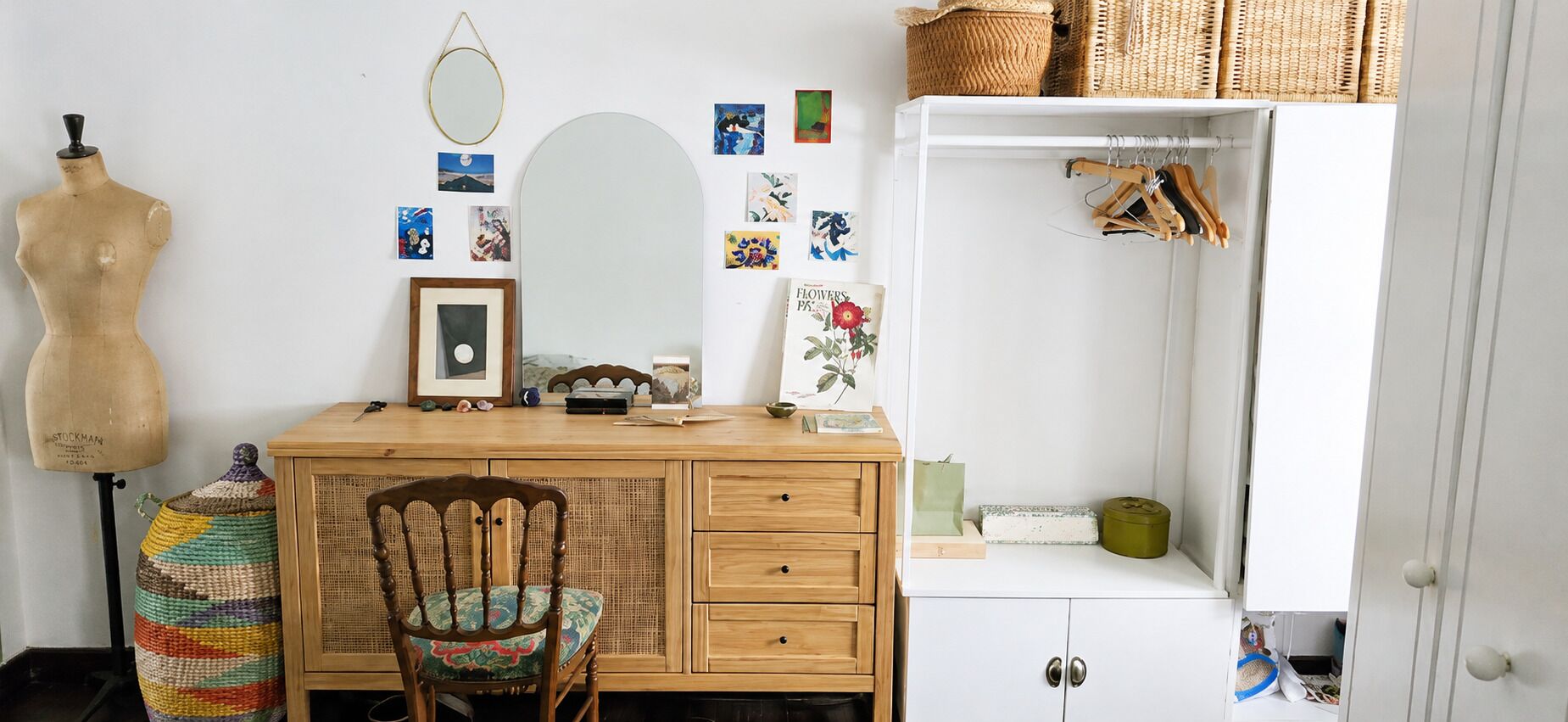 Ein Zimmer mit Schreibtisch aus Holz, einem Sessel, einer Puppenmannequin, einem Spiegel und einem Kleiderschrank mit darin befindlicher Kleidung.