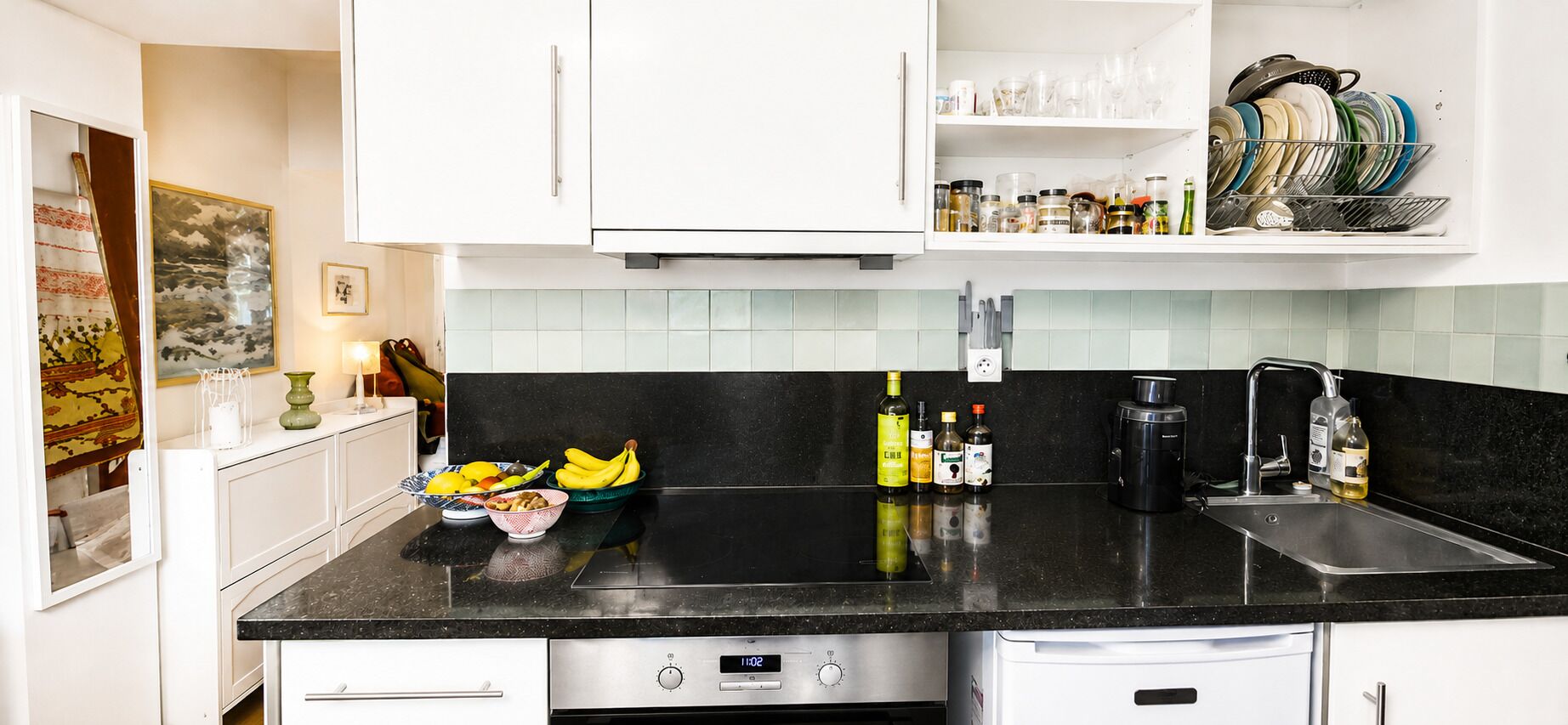 Een keuken met een zwart aanrecht, roestvrijstalen apparatuur en een betegelde achterwand.