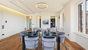 Een moderne eetruimte met een ronde tafel, grijze beklede stoelen en een houten vloer.