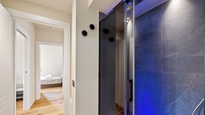 Een hal met een bed, een doucheruimte met blauwe verlichting, en een houten vloer.
