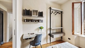 Een slaapkamer met een bed, een bureau met stoel, een kledingrek en planten op planken.