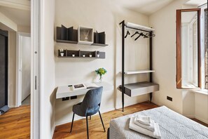 Ein Schlafzimmer mit einem Bett, einem Schreibtisch mit Stuhl, einem Kleiderständer und Regalen mit Pflanzen.