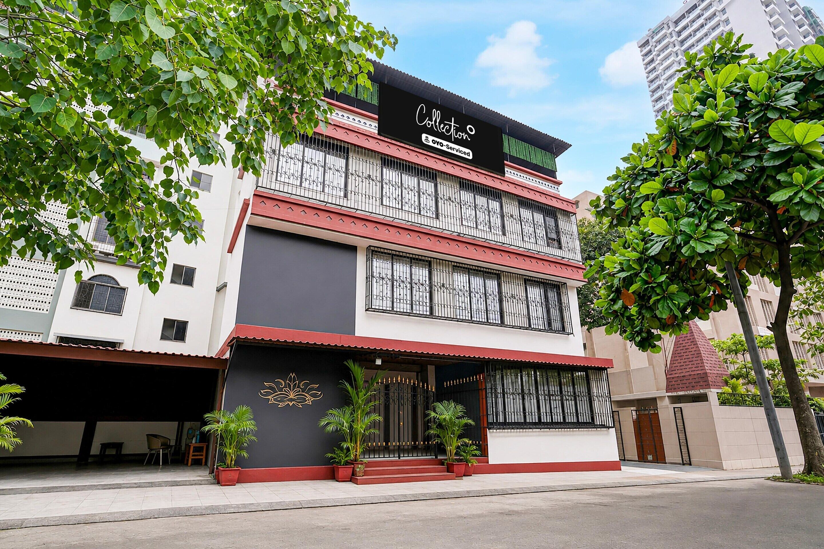 A two-story building with a black and white facade, a sign indicating it is a serviced collection hotel, and a gated entrance with potted plants.
