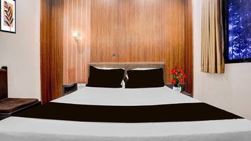 A hotel room with a large bed, wooden paneling on the walls, a nightstand with a lamp, and a window with curtains.