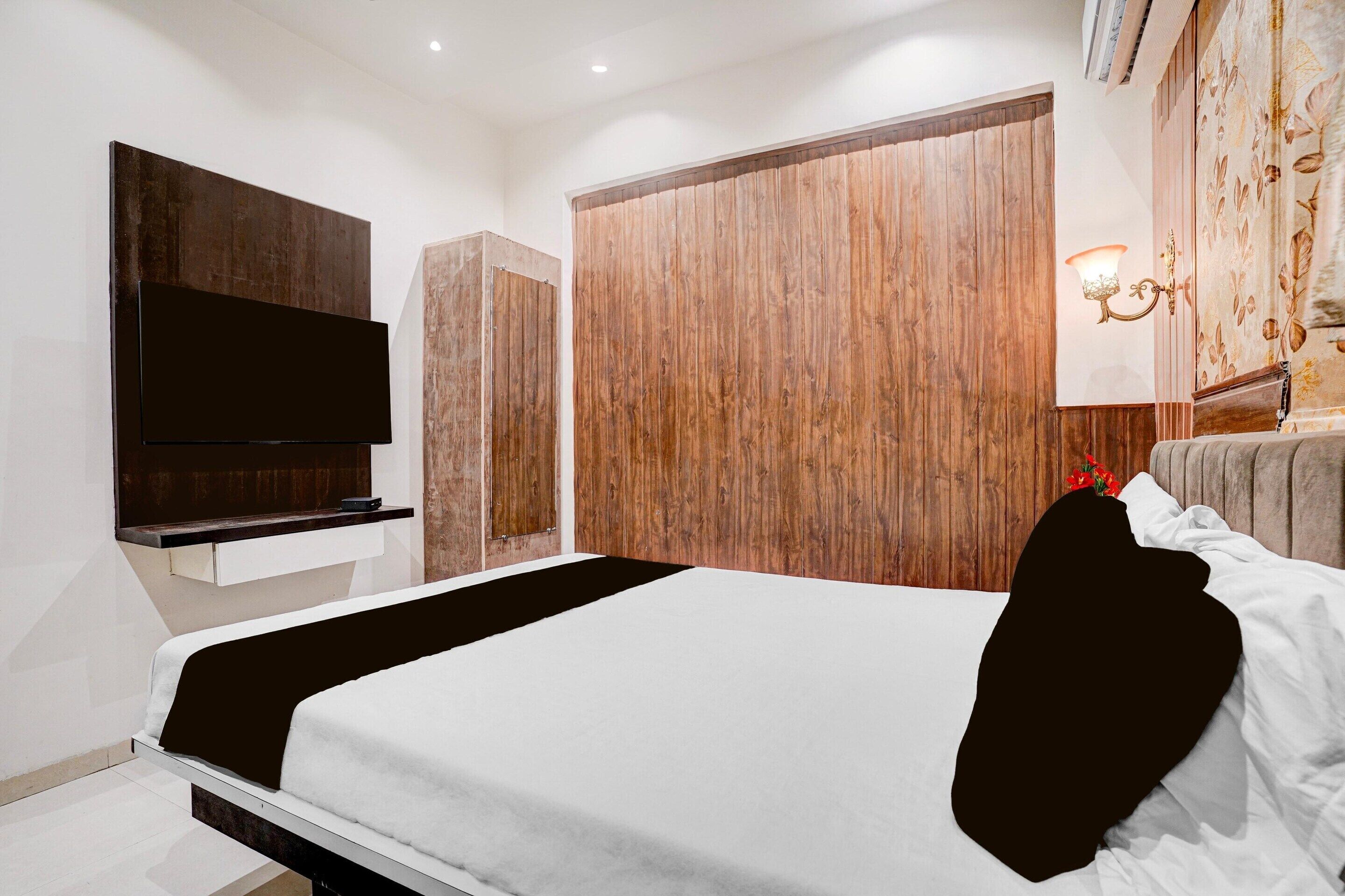 A modern bedroom with a bed, a flat-screen TV mounted on the wall, a wardrobe, and a decorative wall lamp.