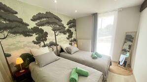A bedroom with two beds, a nightstand, a lamp, a mirror, and a wall mural. - Charming house near castles - 4 guests (Orbigny)