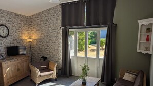 Una habitación con pared de ladrillo, un mueble de madera con televisor, mobiliario de mimbre, una mesa de madera y un ventanal con cortinas.