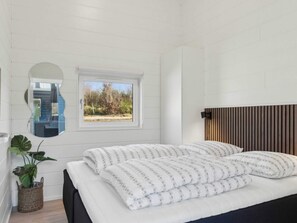 Ein Schlafzimmer mit einem Bett, einem Fenster, einem Spiegel und einer Pflanze.