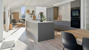 Een moderne keuken met een centraal eiland, inbouwapparatuur en een eethoek met een houten tafel en stoelen.