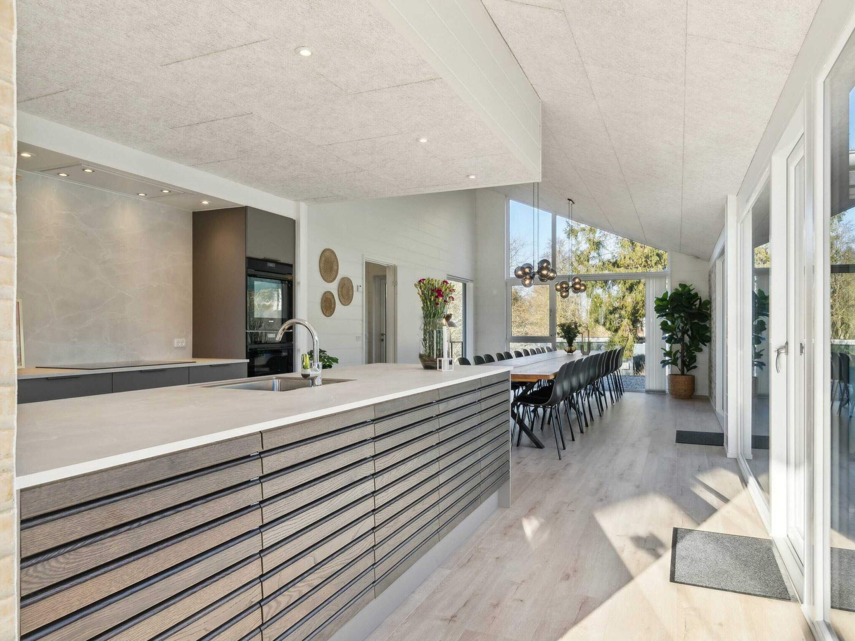 A modern kitchen with a built-in oven, a long counter, and a dining area with a large table and chairs.