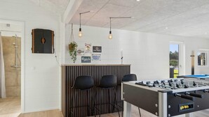 Een kamer met een tafelvoetbaltafel, een bar met krukken, en een douche.