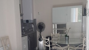 Una cocina compacta con comedor, que incluye una mesa redonda y sillas, un ventilador y un refrigerador.