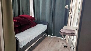 Una habitación compacta con una cama, una pequeña mesa con tabla de planchar y una lámpara.