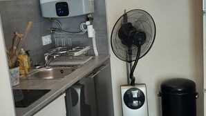 Una cocina compacta con estufa integrada, un ventilador de pared y un cesto de basura.