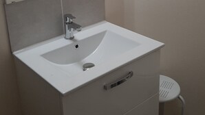 Un baño con un lavamanos blanco, un espejo y un pequeño taburete.