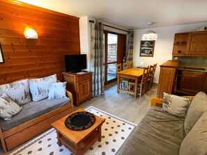 A cozy living room with a sofa, a coffee table, a TV, and a dining area with chairs and a table. - Cozy apartment - 6 guests (Valloire)