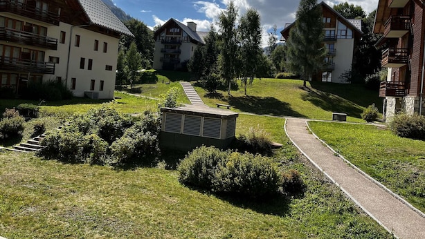 Een rij chalets met balkons, een geplaveid pad en een gazon met bomen.
