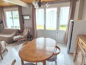 A room with a wooden dining table, a covered sofa, a chair, a small table with a lamp, and a refrigerator. - Quiet house, pets allowed - 4 guests (Cucq-Stella Plage)