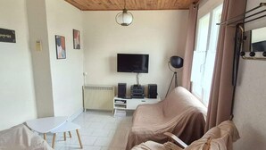 Una sala de estar con techo de madera, un televisor, un radiador y una ventana con cortinas.
