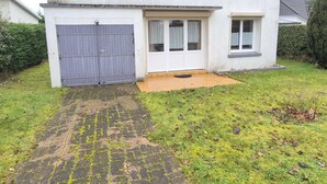 Una casa de dos pisos con cochera delantera, un pequeño porche y entrada pavimentada.