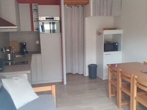 Une cuisine compacte équipée d’un réfrigérateur, d’un four et d’un four à micro-ondes. On y trouve une table à manger avec des chaises et une petite poubelle.