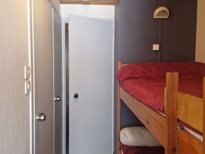 Une chambre avec un lit superposé, une porte et un luminaire fixé au mur.
