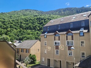 Un immeuble à plusieurs étages, doté d’un toit plat, de nombreuses fenêtres et offrant une vue sur une colline boisée.