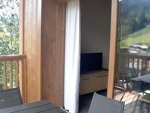 Ein Balkon mit Holzgeländer, ein Fernseher auf einem Standfuß und eine Schiebetür aus Glas.
