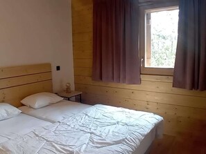 Ein holzgetäfeltes Zimmer im Blockhausstil mit einem Bett, einem kleinen Tisch mit Lampe und einem fenster mit Vorhängen.