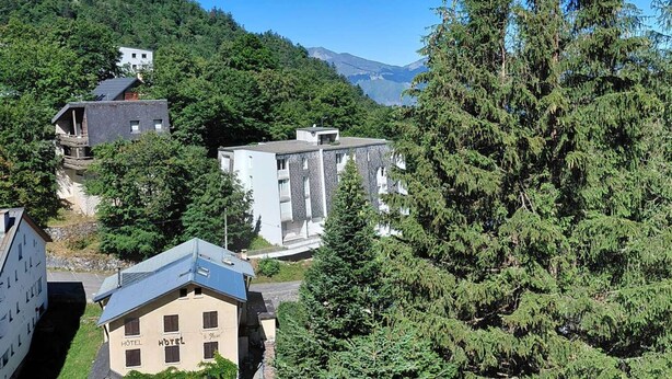 Um hotel com fachada de pedra, varanda e vista para uma encosta arborizada.